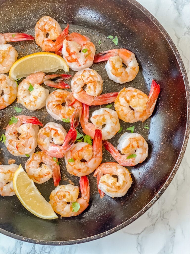 Overhead photo of cooked shrimp in a pan with lemon slices and parsley