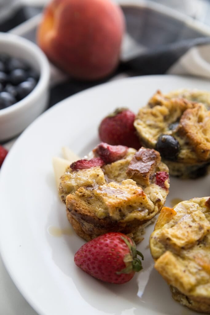 A close up of mini french toast casserole cups on a round white plate garnished wit berries 