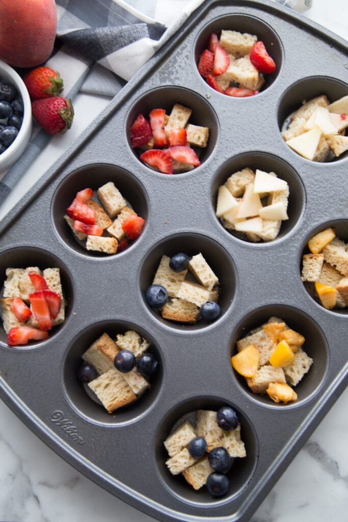 A muffin tin filled with healthy french toast casserole cups topped with various fresh fruit toppings