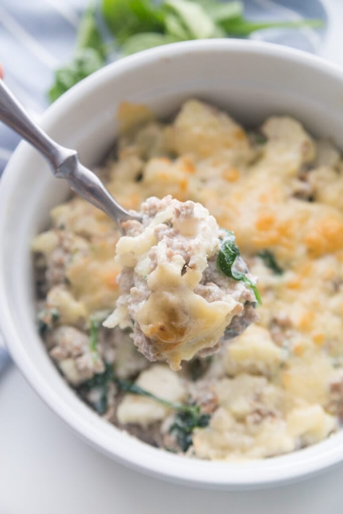 A white ceramic bowl with sausage and cauliflower casserole made with ricotta and parmesean cheese 