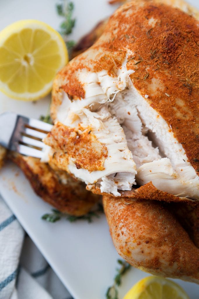 A close up of Spice Rub Chicken made in the Instant Pot on a white plate sitting near a slice of lemon and some fresh thyme. 