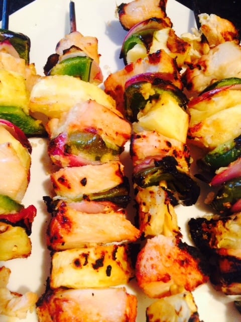 Diced chicken, pineapple, green pepper, and red onion are threaded on skewers and grilled, laying in a line on a plate