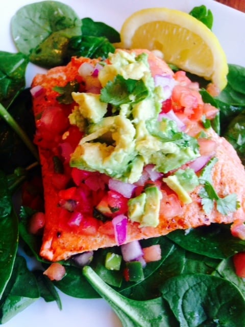 Southwest Salmon over spinach topped with diced ed onion, fresh salsa, cilantro, and avocado with a lemon wedge on the side