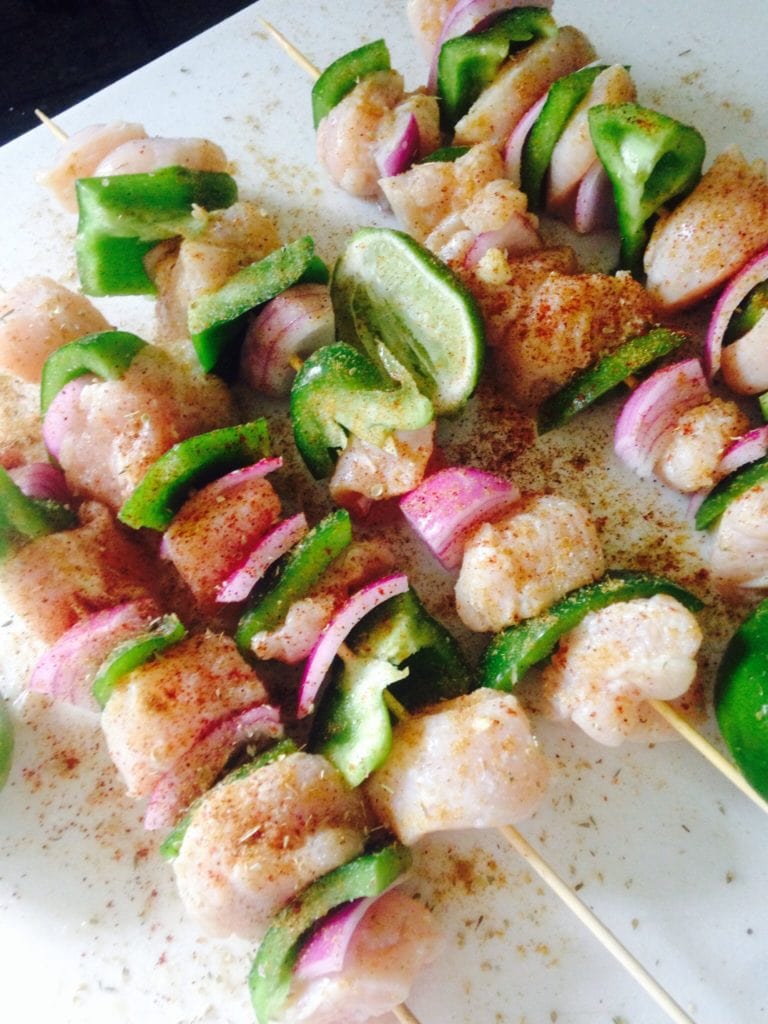 raw diced chicken, green peppers, and red onions on skewers with lime and seasoning