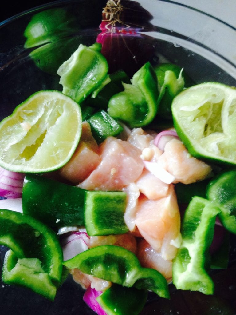 raw diced chicken, green peppers, and red onion in a bowl marinating in lime juice