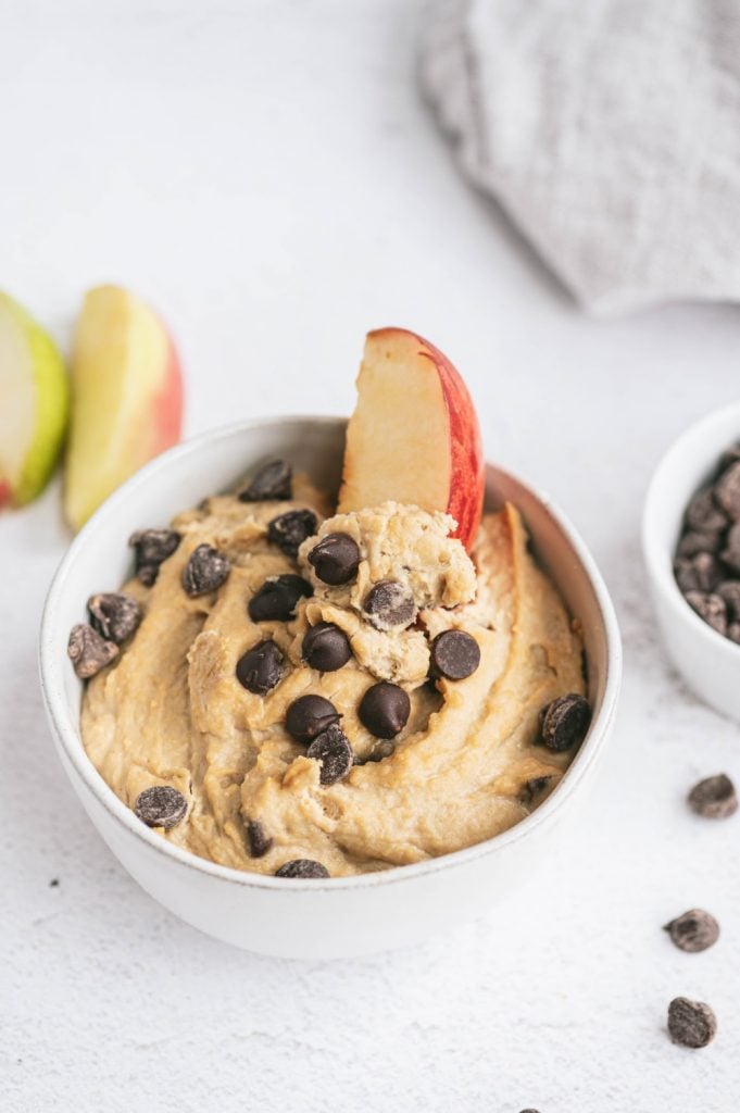 A apple slice dipped into a bowl of cookie dough dip made with chickpeas