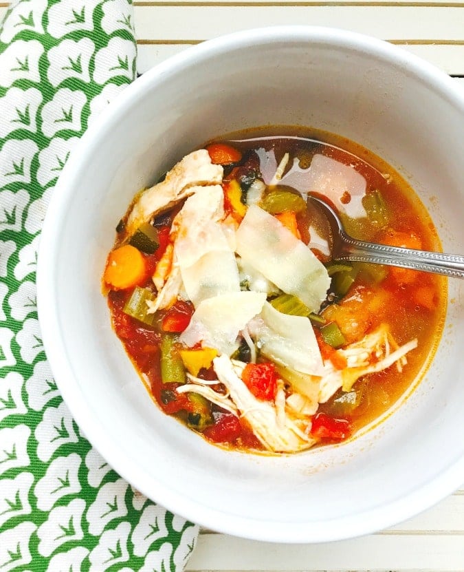 Overhead photo of Chicken veggie soup in a white bowl with a spoon inside