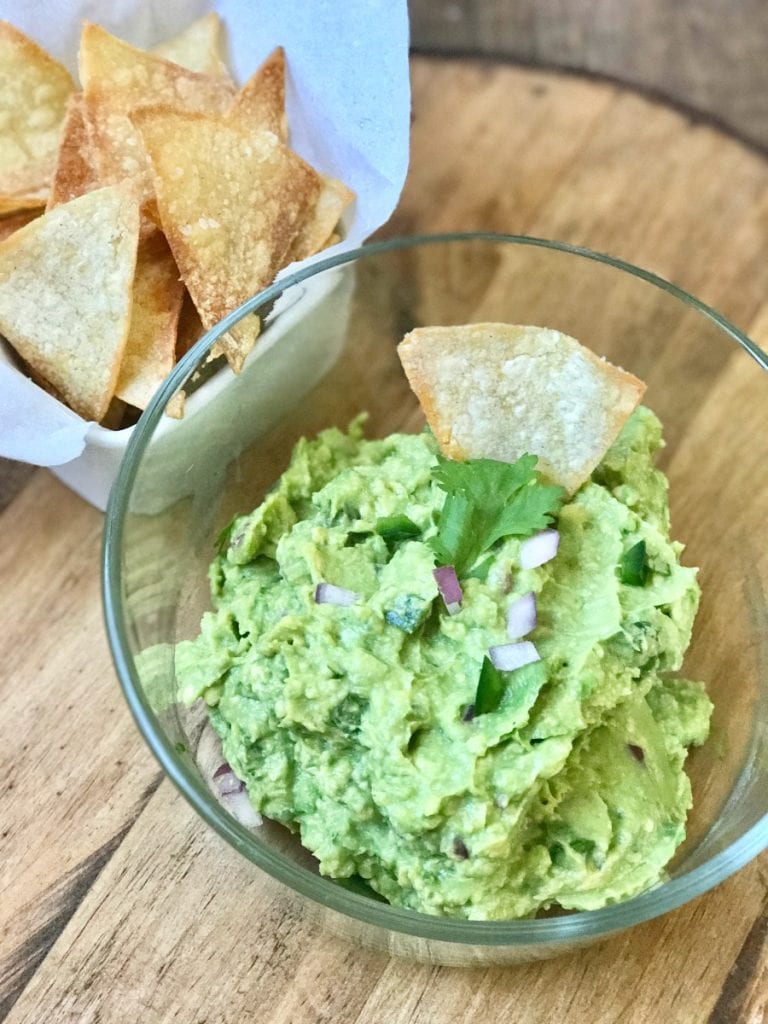 A glass bowl of 21 Day Fix Guacamole with a side of homemade chips on top of a wooden surface | Confessions of a Fit Foodie