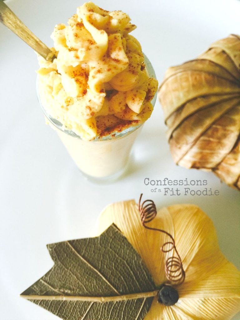 Overhead photo of pumpkin frosting in a small glass next to pumpkin decorations.