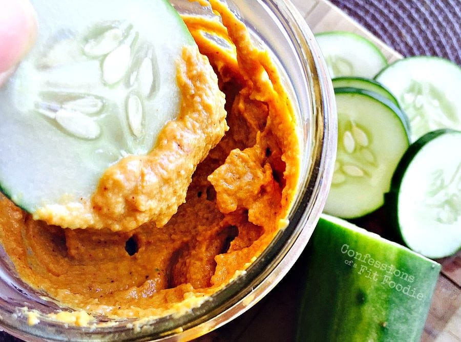 Overhead photo of cucumber being dipped into pumpkin hummus. Cucumber slices line the side.