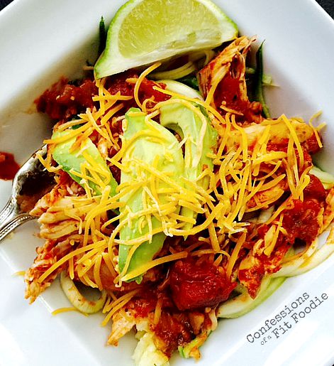 A square bowl filled with salsa lime chicken over zoodles, topped with avocado, shredded cheese and lime.