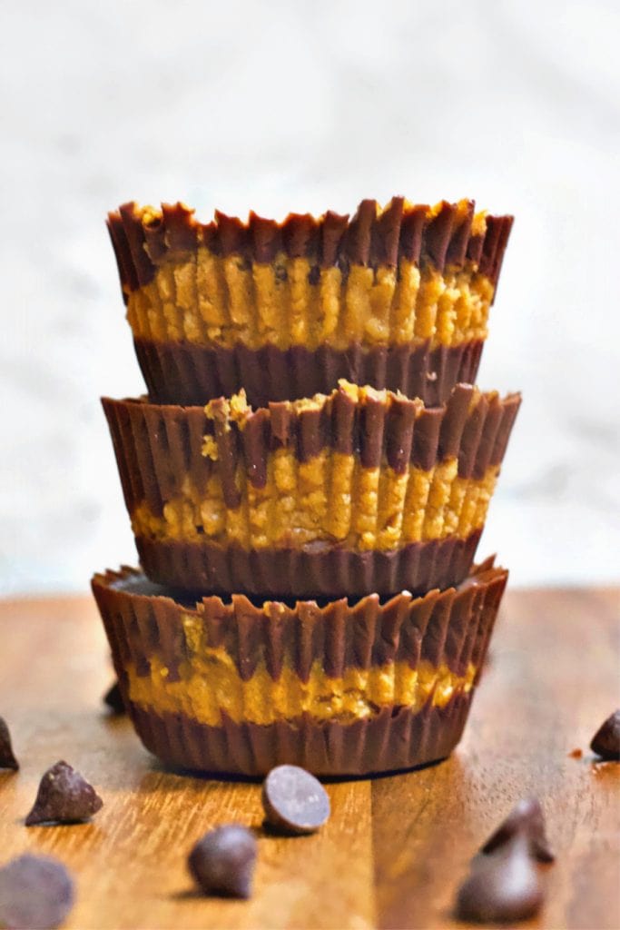 Three chocolate pumpkin cups stacked up on a table with chocolate chips sitting nearby. 
