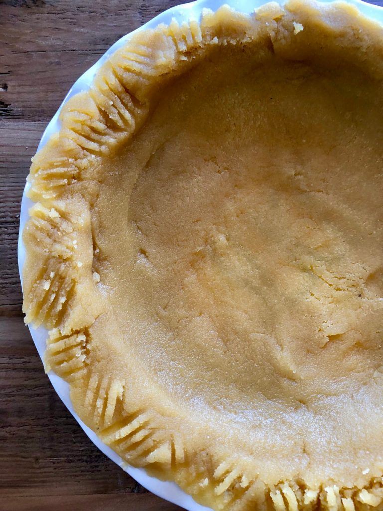 Almond Flour Pie Crust in a pie plate set on a wooden backdrop