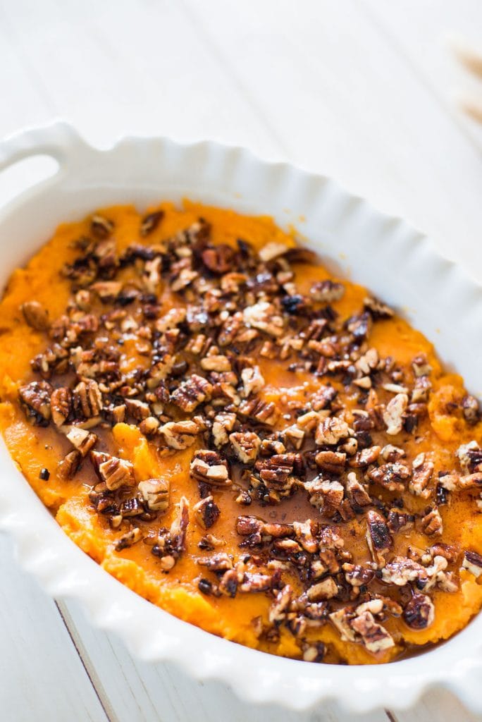 White casserole dish with a 21 day fix healthy sweet potato casserole topped with pecans on a white wooden table. 