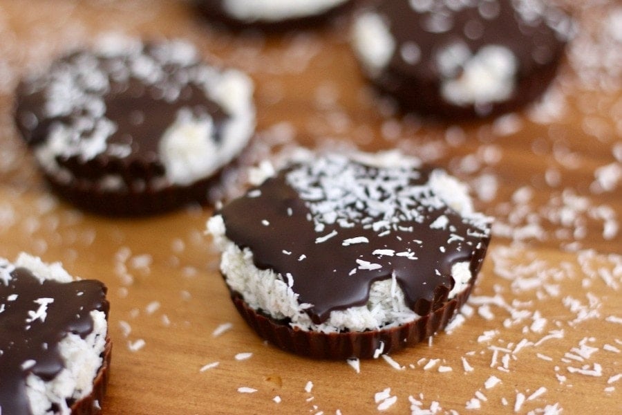 Close up view of homemade chocolate coconut candy cups. There is coconut sprinkled on the wooden tabletop.