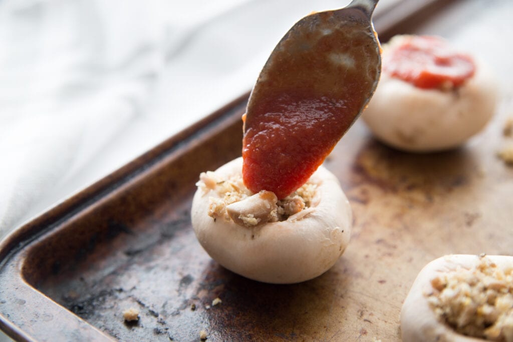 An Italian Style Stuffed Mushroom being topped with homemade tomato sauce before baking