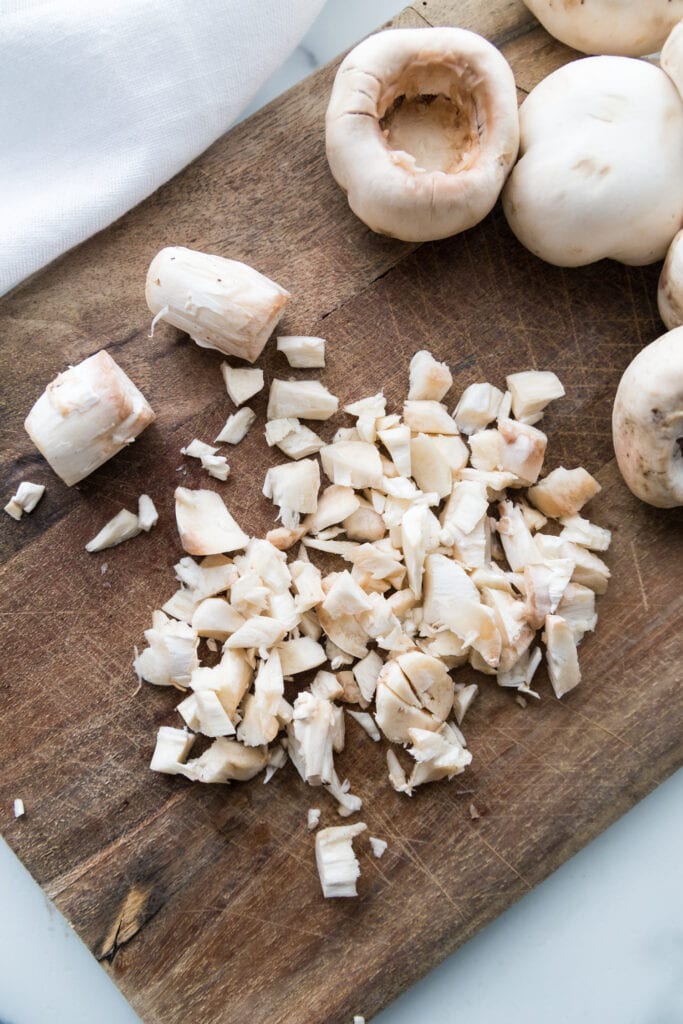 Chopped mushrooms stems for stuffed mushrooms on a wooden cutting board