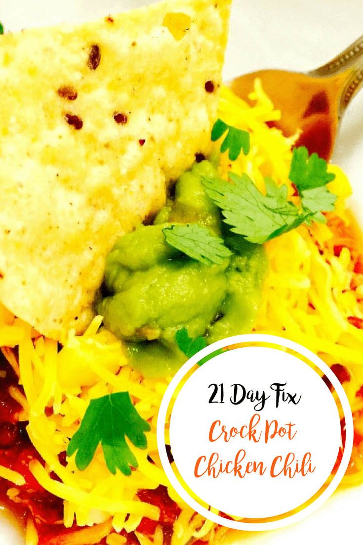 Crock Pot Chili Chicken topped with cheddar cheese, cilantro, avocado, and a single chip dipped in the middle. A fork is resting on the side of the bowl with the text overlay- 21 Day Fix Crock Pot Chicken Chili