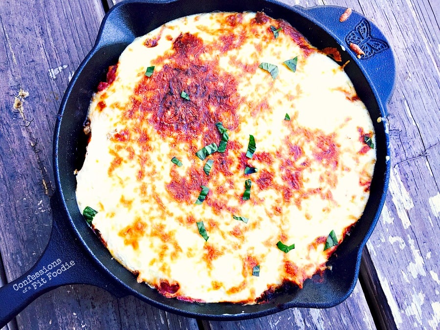 Overhead view of cast iron skillet filled with butternut squash lasagna. The top cheese layer has been broiled to a golden brown and garnished with basil.