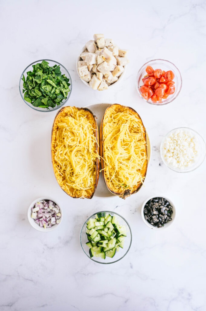 Overhead image of roasted spaghetti squash and glass bowls of Mediterranean inspired toppings