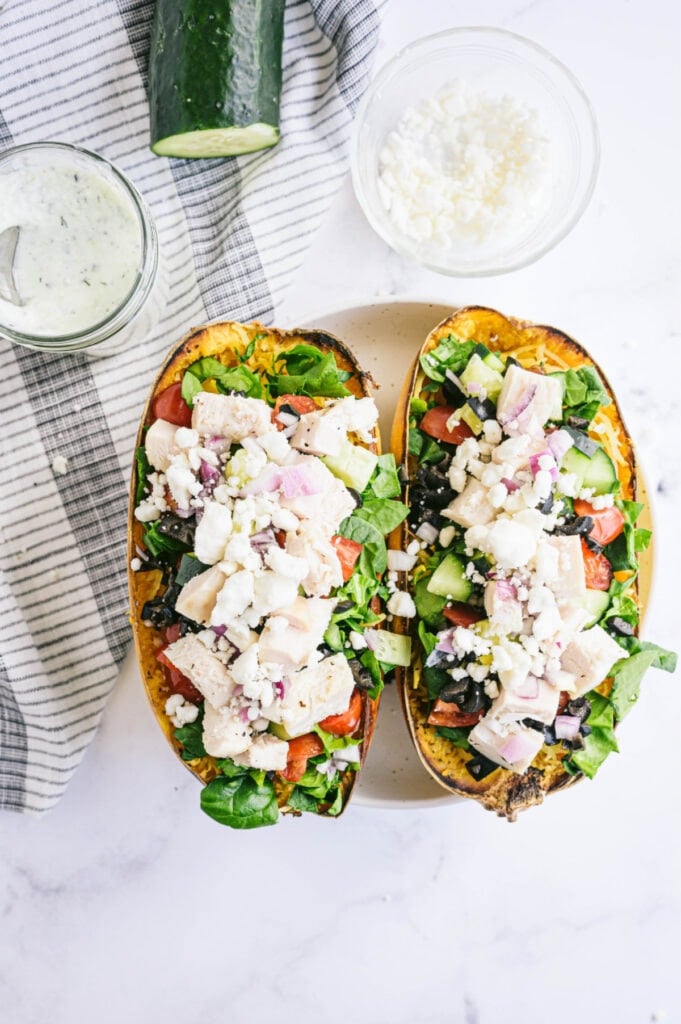 Overhead image of veggie stuffed spaghetti squash topped with chicken and feta cheese. Homemade Tzatziki sauce is in a dish on the side.
