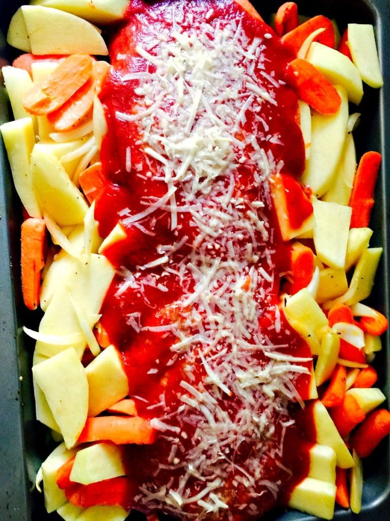 Overhead photo of a metal baking dish with a row of sliced potatoes and carrots on each side. Down the middle is a row of meatloaf- 2 separate loves, topped with tomato sauce and shredded cheese.