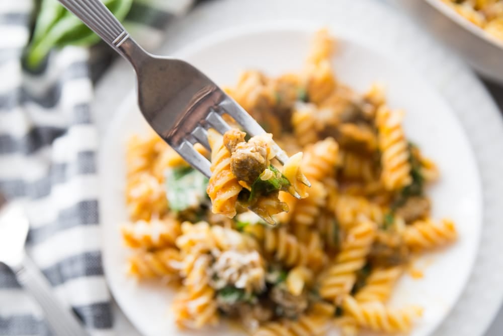 A close up of a fork over a plate of pumpkin pasta with spicy sauce and spinach