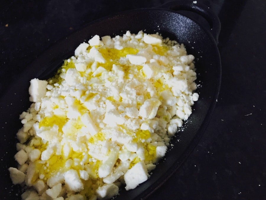 Feta cheese topped with olive oil in a cast iron pan