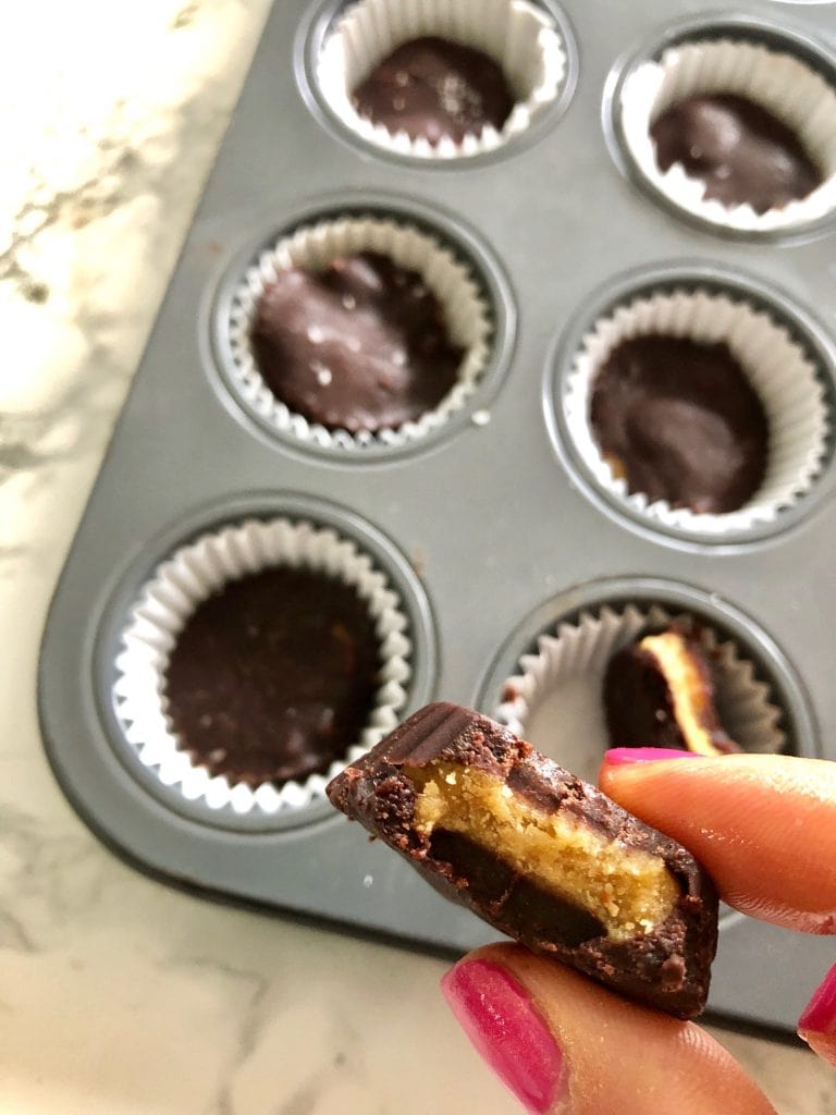 A close up of a mini homemade peanut butter cup, a whole mini muffin tray is in the background filled with finished peanut butter cups