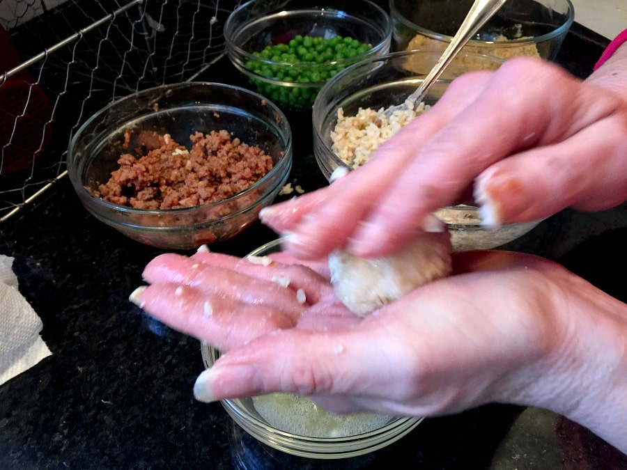Hands in motion rolling mini arancini rice balls with glass bowls filled with ingredients in the background