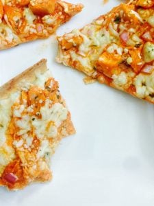 Buffalo chicken flatbread pizza cut into triangles on a white background. One of the triangles has bites taken out of it.