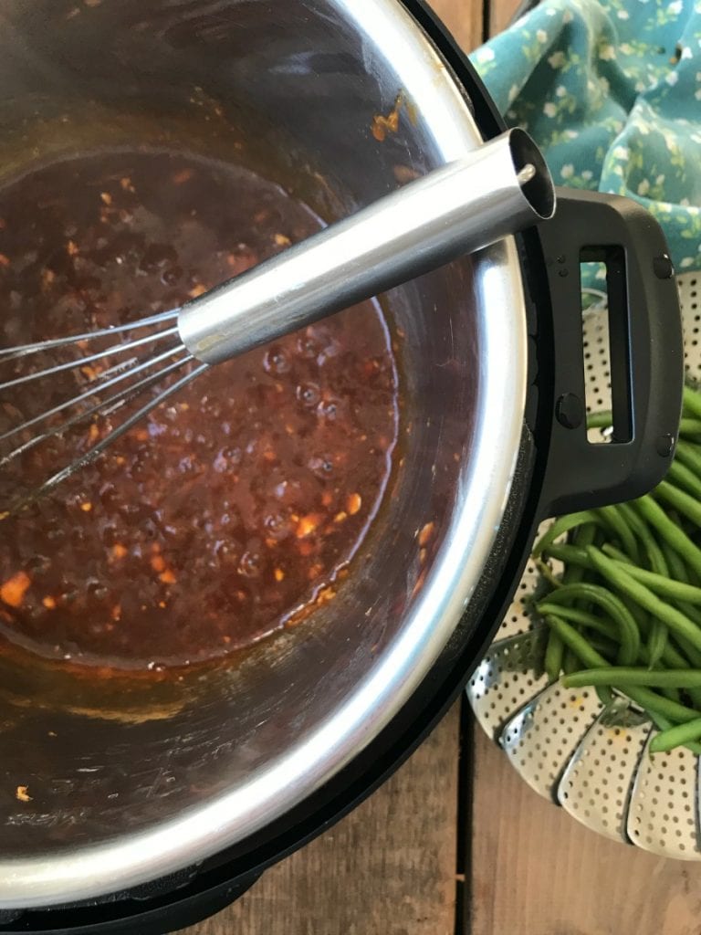 Overhead photo of Asian Chicken sauce in process with a whisk, and steamer basket of green beans on the side