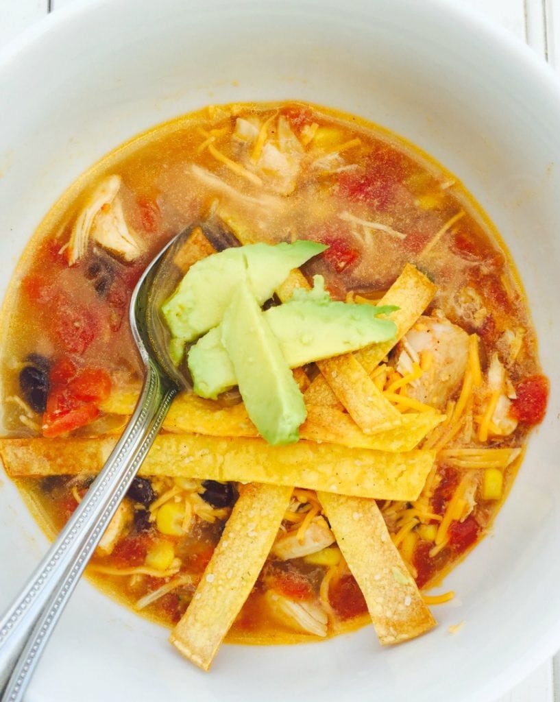 Close up photo of a bowl of chicken tortilla soup topped with diced avocado and homemade tortilla strips.