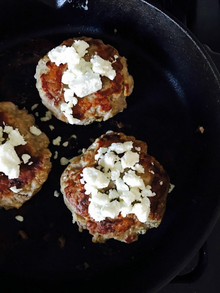 Easy Turkey Burgers topped with goat cheese cooking in a cast iron pan.
