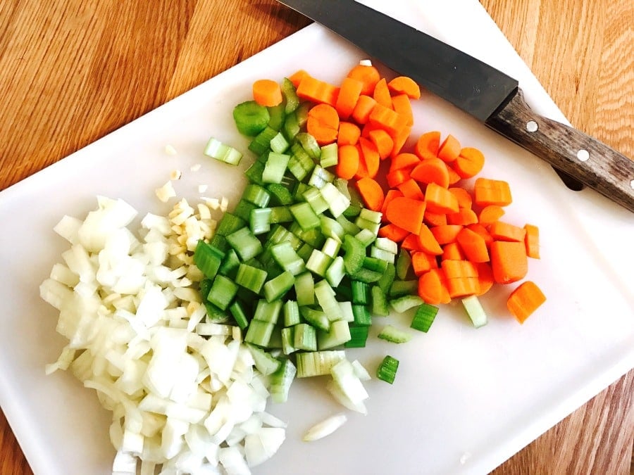 Chopped veggies on a white cutting board with a chef's knife on the side.