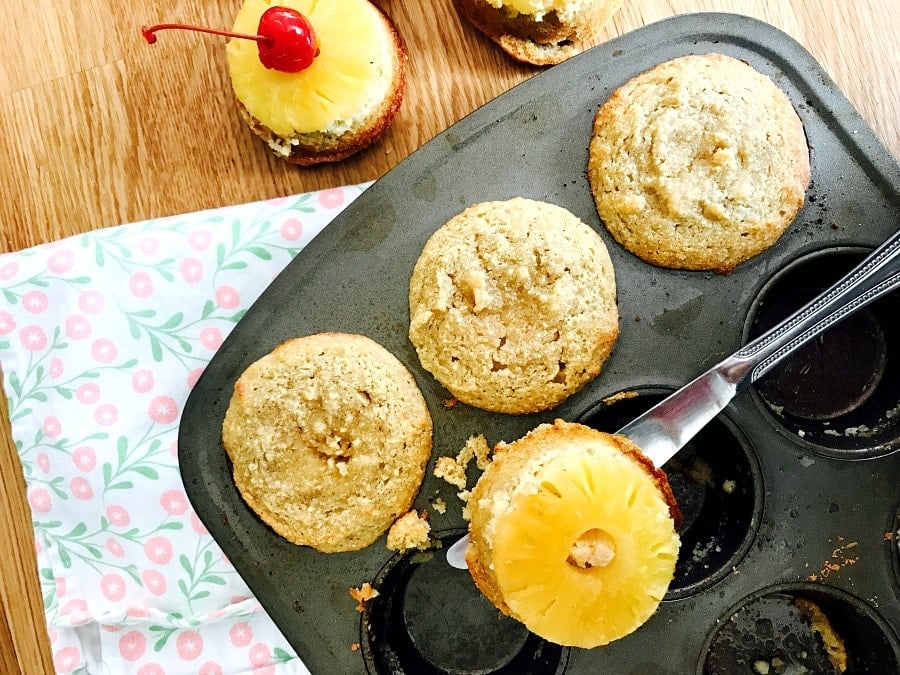 A knife removing pineapple upside down cupcakes from a muffin tin.