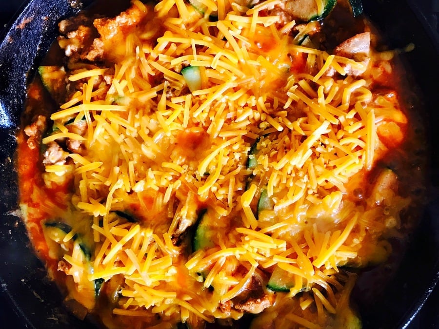 Cast Iron skillet filled with lean meat, zucchini, enchilada sauce, and topped with shredded cheddar cheese
