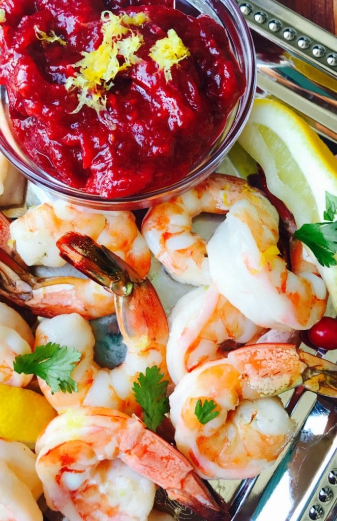 Close up of Roasted Shrimp on a silver platter with Cranberry chutney in a glass bowl. Lemon wedges and cilantro for garnish.