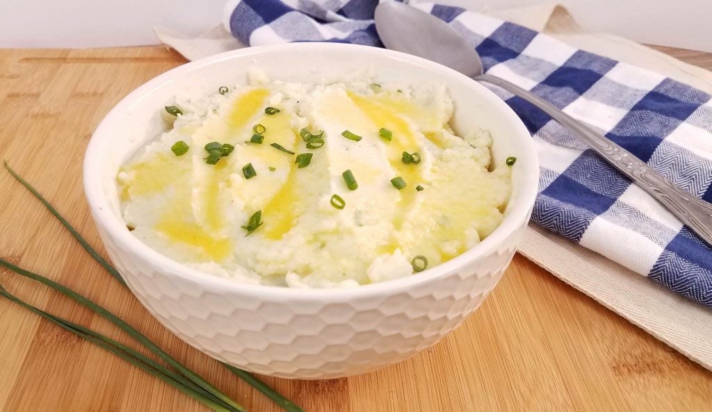 Whipped cauliflower mash in a white serving bowl with melted butter and chives on top.