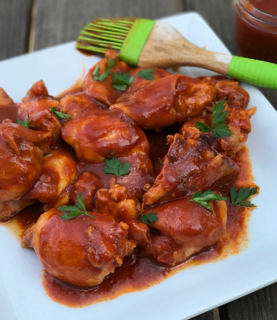 BBQ chicken thighs on a white plate with a green sauce brush on the side.