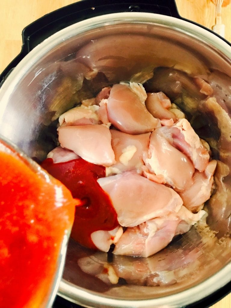 Raw chicken thighs in an instant pot with homemade bbq sauce being poured on top.