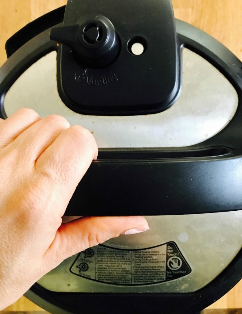 Overhead photo of an instant pot lid with a person's hand on the handle