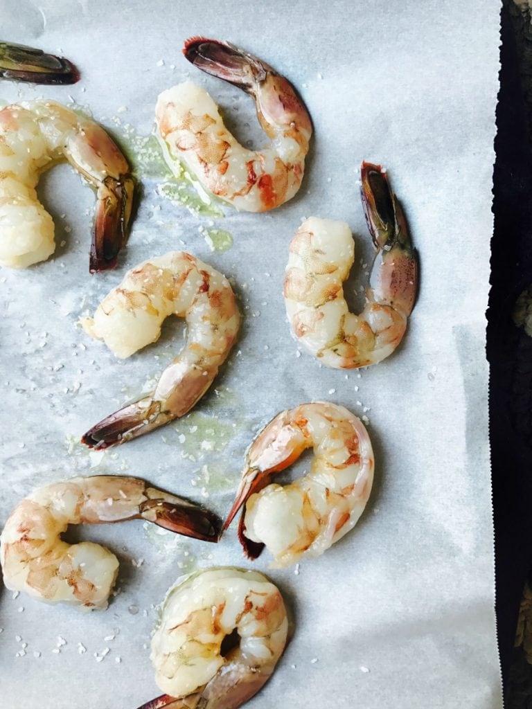 Raw shrimp drizzled with olive oil and salt on a parchment lined sheet pan