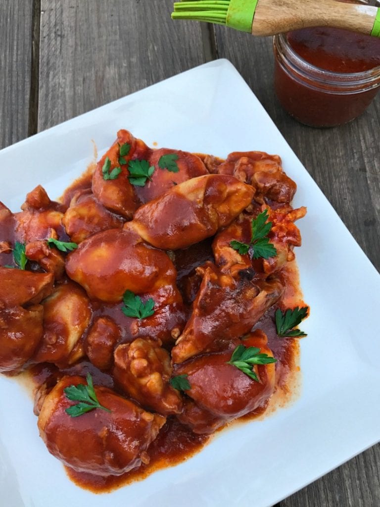 Maple BBQ chicken thighs on a white plate with BBQ sauce and a brush in the background.