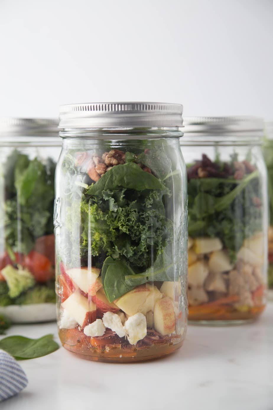 Mason jar salads with dressing, veggies, cheese, and kale. 