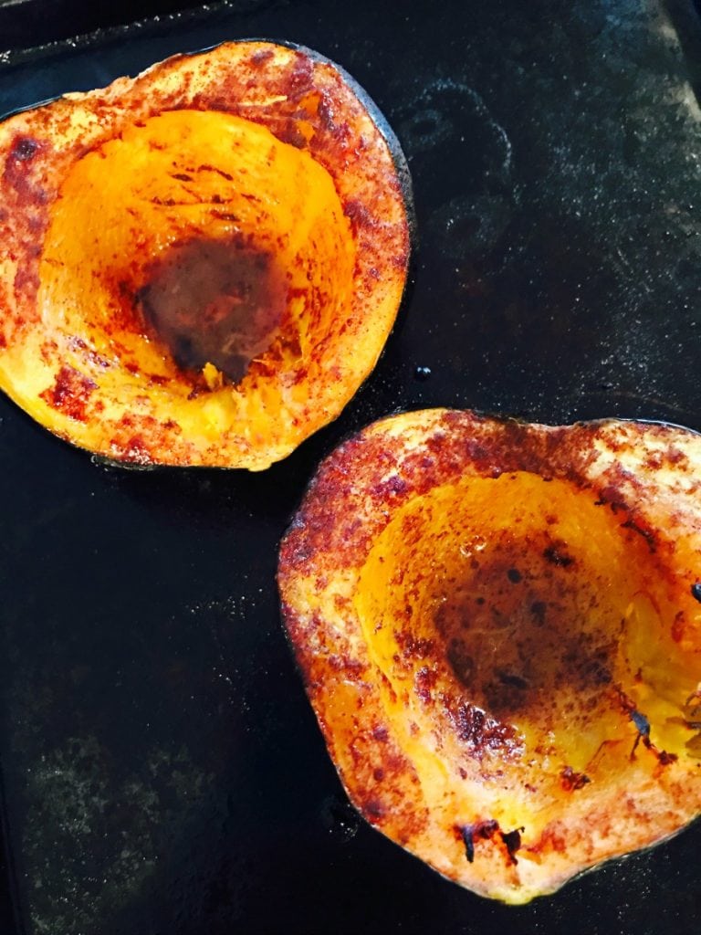 An acorn squash is cut in half and on a roasting pan. The squash is nice and caramelized brown on the inside.