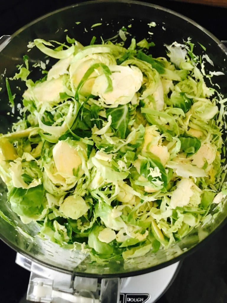 Overhead view of shaved Brussels sprouts in a food processor with the lid off.