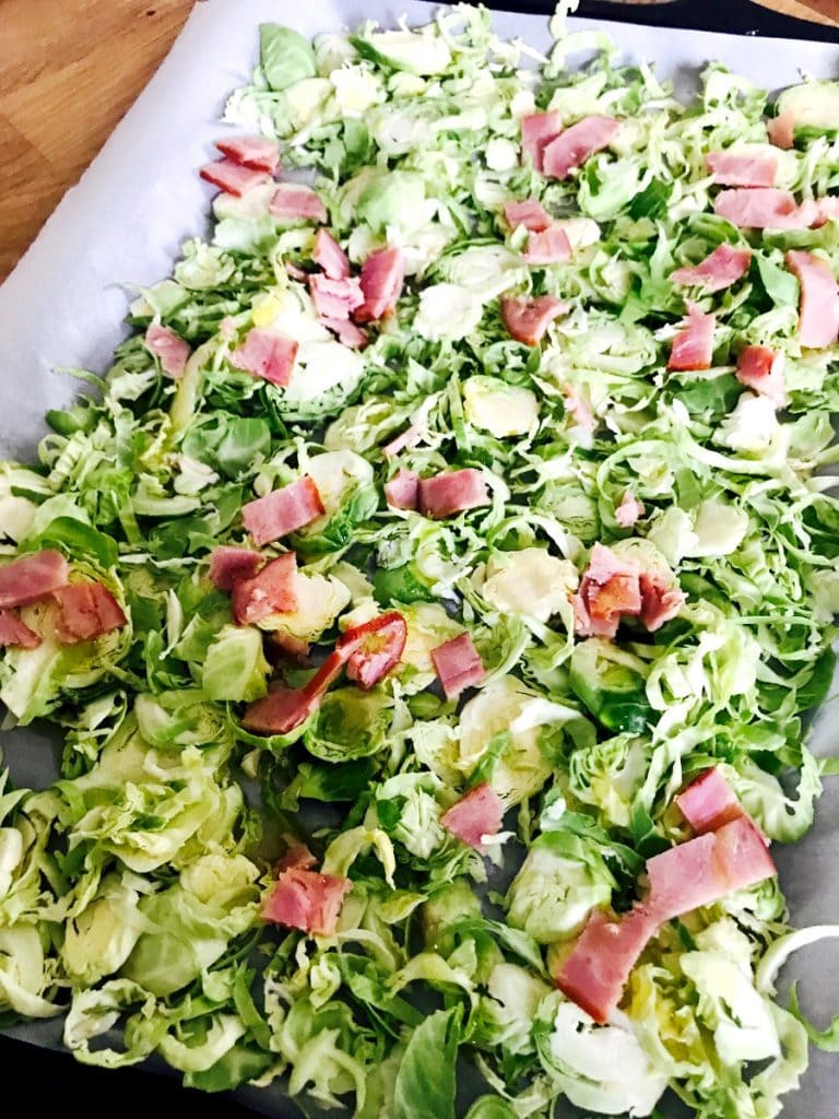 A sheet pan full of uncooked shaved Brussels sprouts and diced turkey bacon.