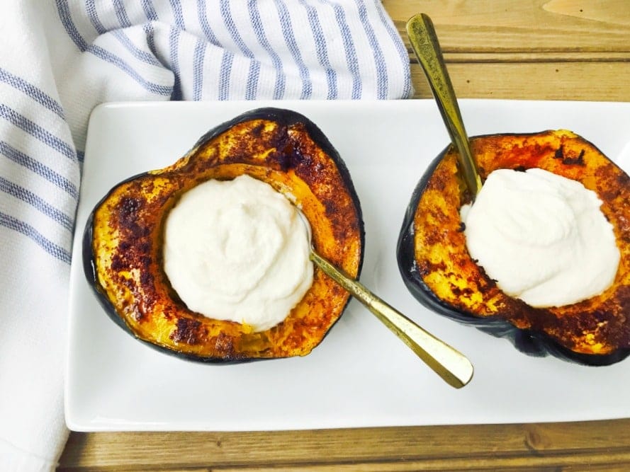 two halves of a roasted acorn squash are sitting on a rectangular plate and stuffed with sweet maple whipped ricotta. There are spoons in each dip, ready to eat!