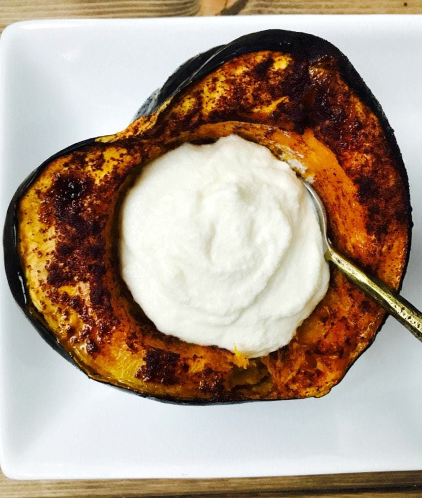 Close up of roasted acorn squash with sweet whipped ricotta filling. The squash resembles a heart shape on a white plate.